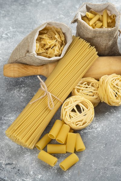 Pasta varieties in rustic basket with a wooden rolling pink on marble background